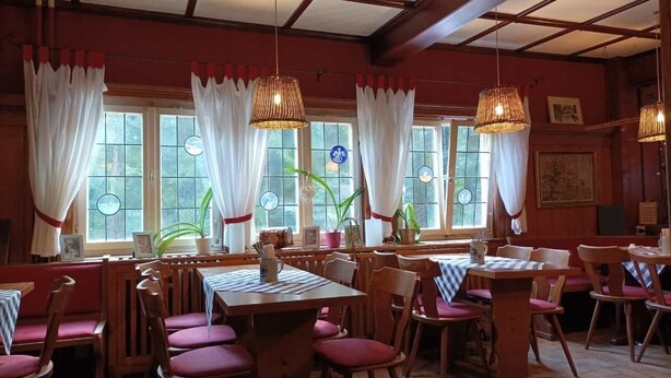 A restaurant interior with wooden tables and chairs, white curtains, and hanging wicker lamps. - Bergwaldhütte  (Bühl)