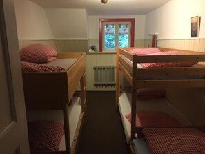 Una habitación de residencia estudiantil con literas, un radiador, una ventana con vistas a árboles y un cuadro en la pared.