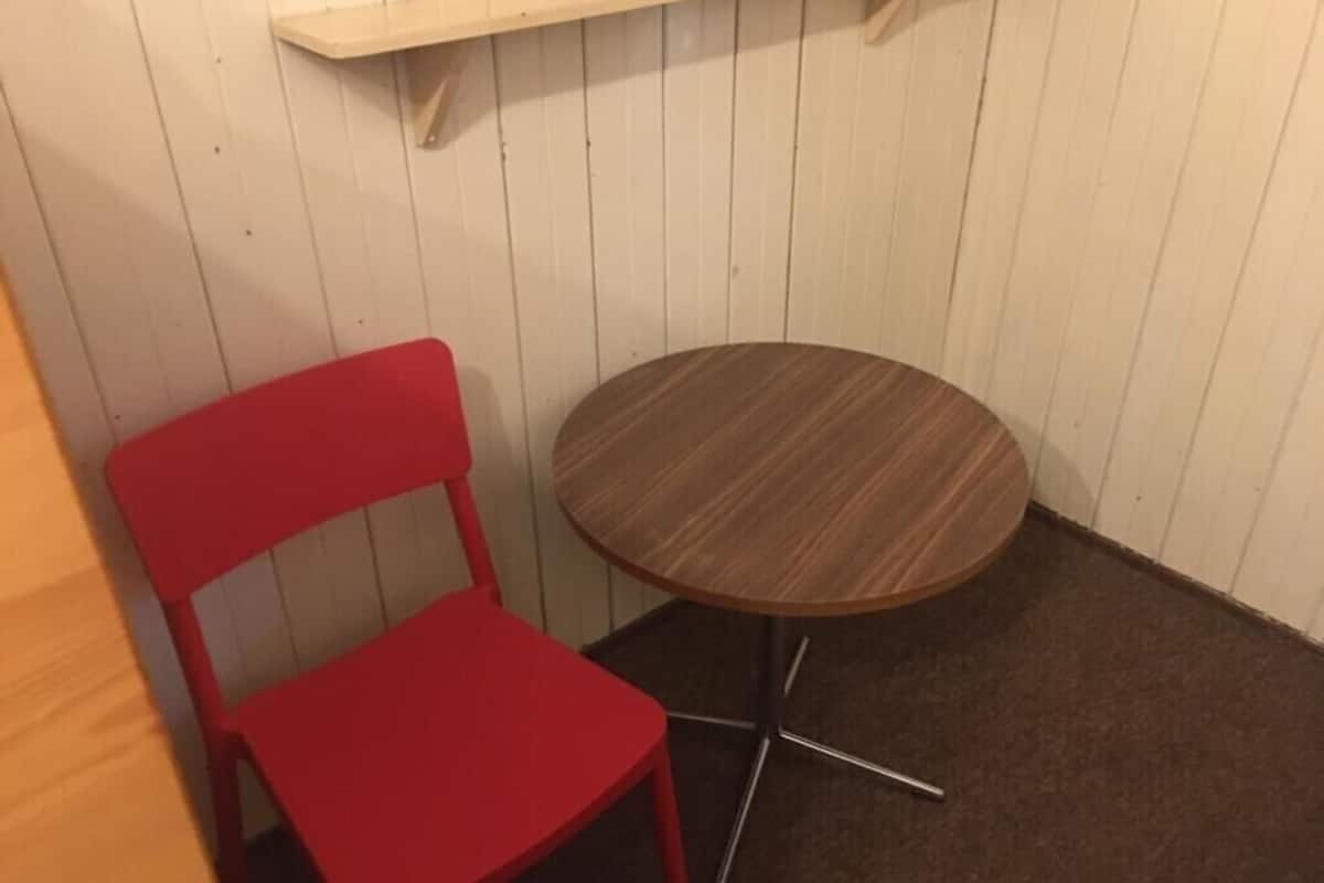 Una habitación pequeña con una mesa redonda de madera y una silla roja.