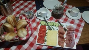 A table with a checkered tablecloth, a plate of food including bread, tomatoes, cheese, and ham, and a basket of bread. - Bergwaldhütte  (Bühl)
