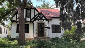 Une maison à deux étages, dotée d’un portail en arc de pierre, et entourée d’une végétation luxuriante.