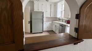 Une cuisine avec des meubles blancs, un réfrigérateur, un évier et un plan de travail en bois.