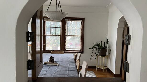 Un couloir doté d’un plafond en arc de cercle, d’un plancher en bois, d’une table à manger entourée de chaises, d’une plante en pot et d’un décor en forme de pomme de pin.