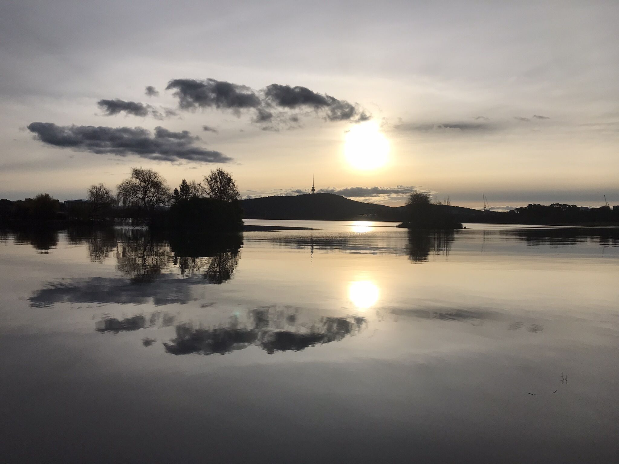 A calm lake with reflections of trees and a distant hill.