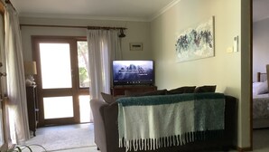Ett vardagsrum med en soffa, en tv, en tavla på väggen och en dörr som leder ut.