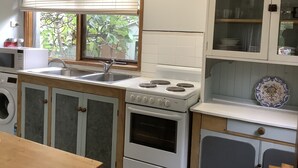 Ett kök med en inbyggd ugn, en mikrovågsugn, en diskho och ett fönster med persienner.