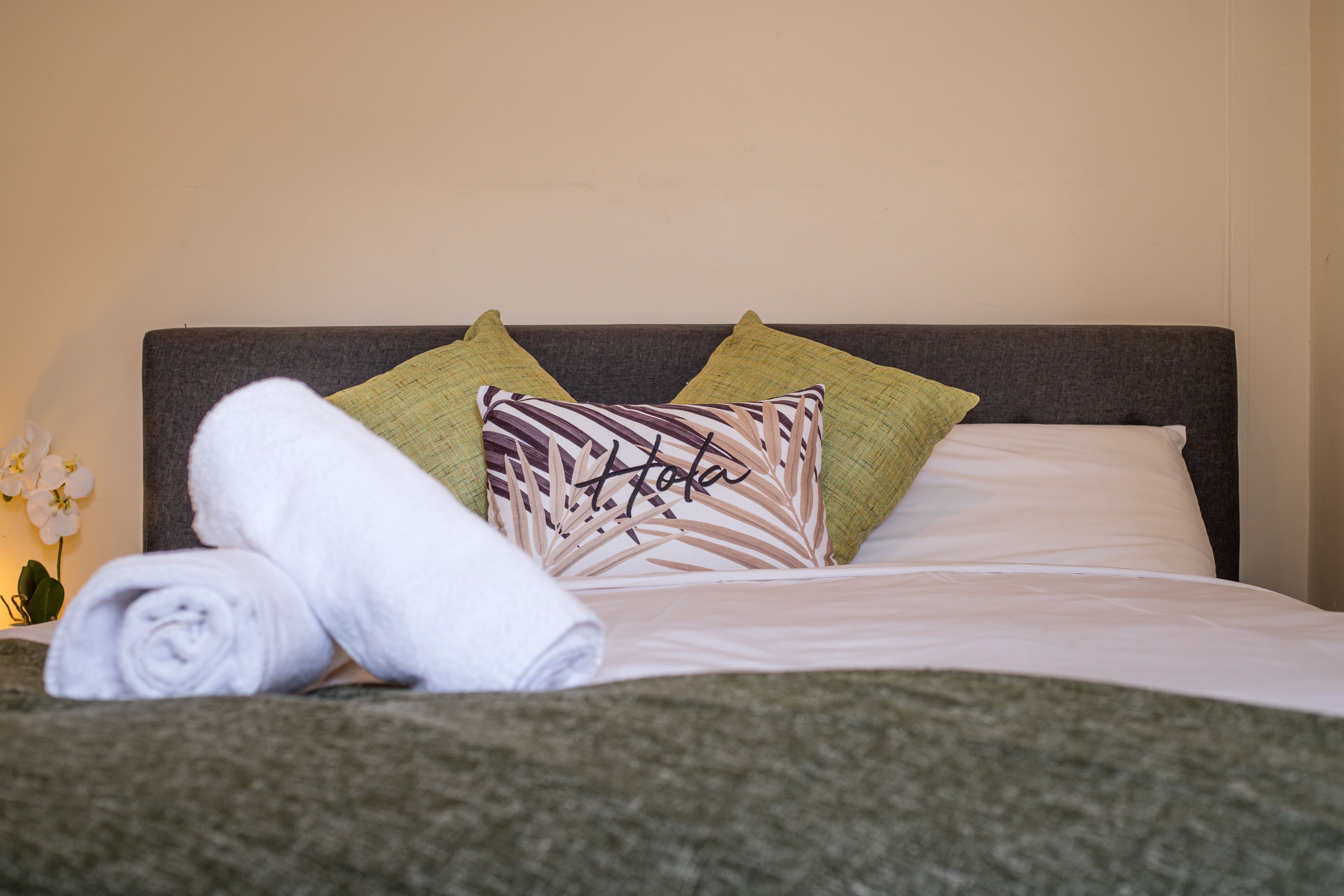 A neatly made bed with a rolled white towel, two pillows, one with a leaf pattern, and a green pillow.