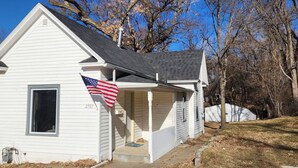 A white single-story house with a gabled roof, a front porch, and an American flag. - Cozy American Style Cottage (Sioux City)