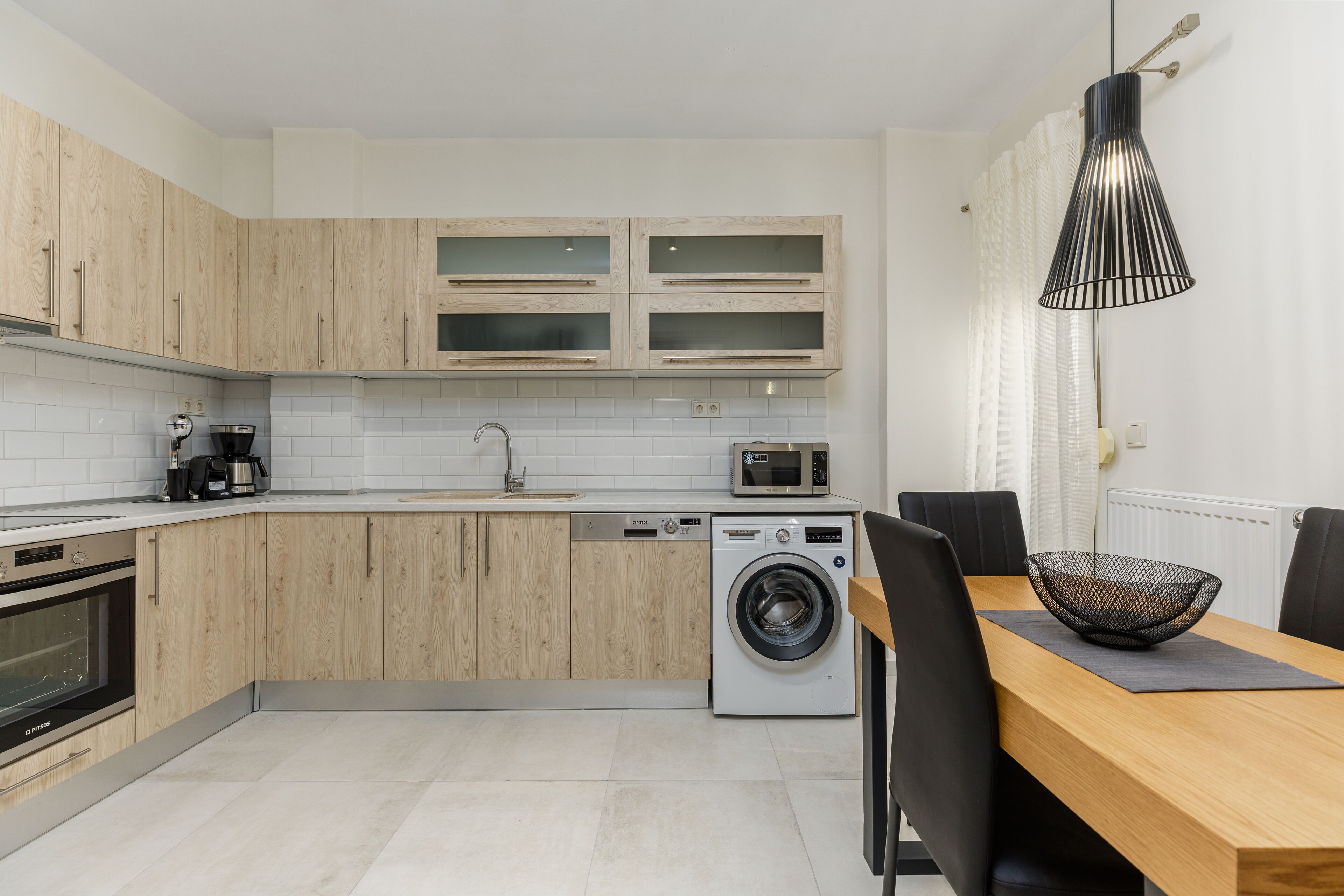 Une cuisine moderne avec des meubles en bois, un lave-linge encastré et un coin repas comprenant une table et des chaises.