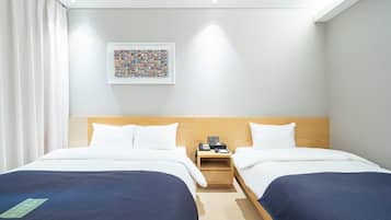 A hotel room with two beds, a wooden headboard, a nightstand with a phone and a book, and a framed picture on the wall.