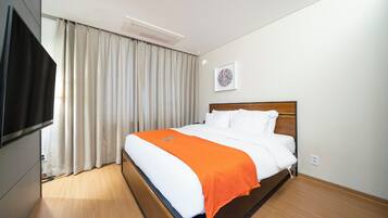 A hotel room with a bed, a TV, a window with curtains, and a wall-mounted artwork.
