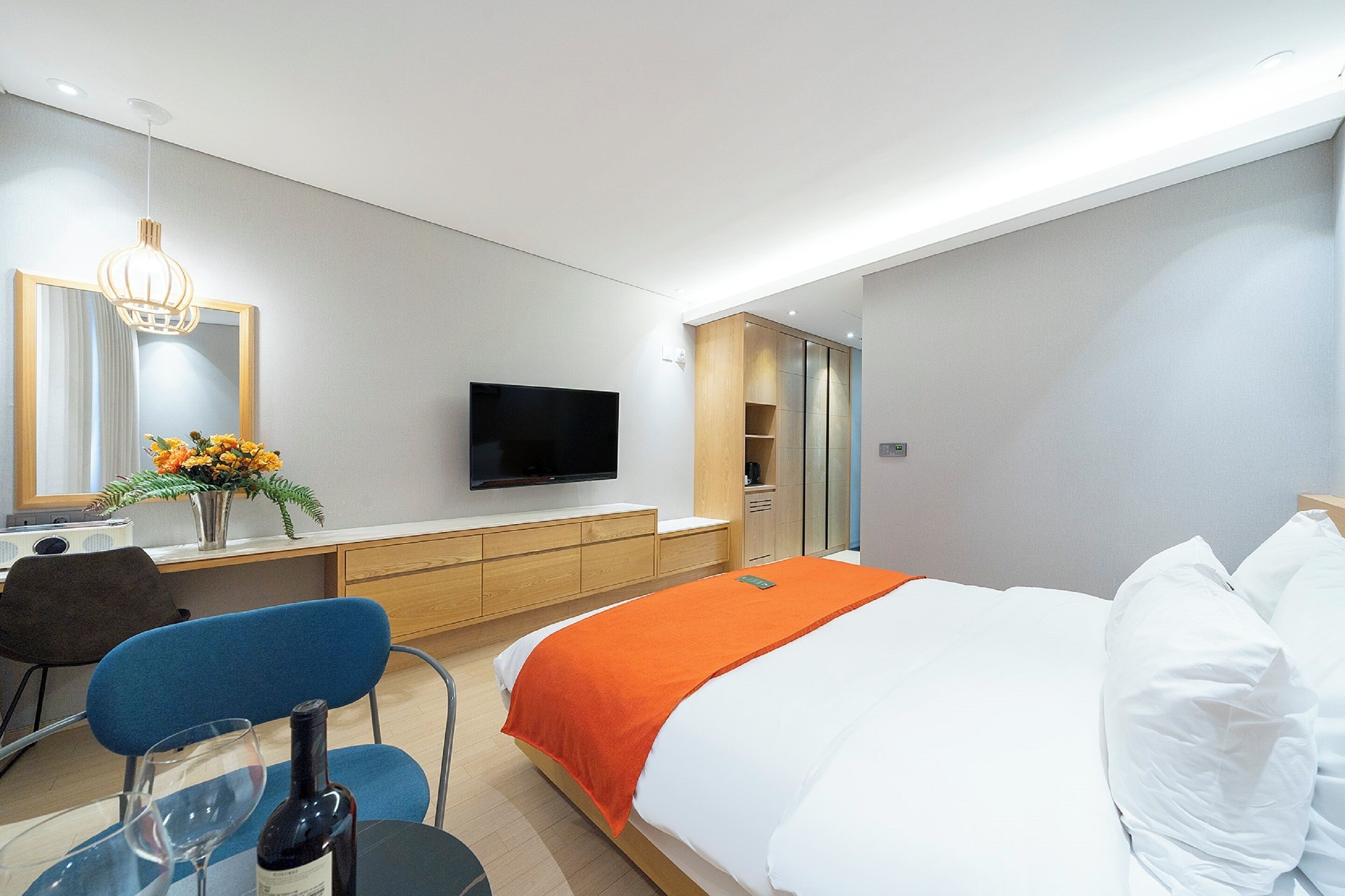 A modern hotel room with a large bed, a flat-screen TV, a desk with a chair, and a mirror.