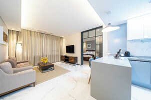 Una sala de estar moderna con un sofá, una mesa de centro y una televisión. Hay una zona de cocina con encimera y armarios.