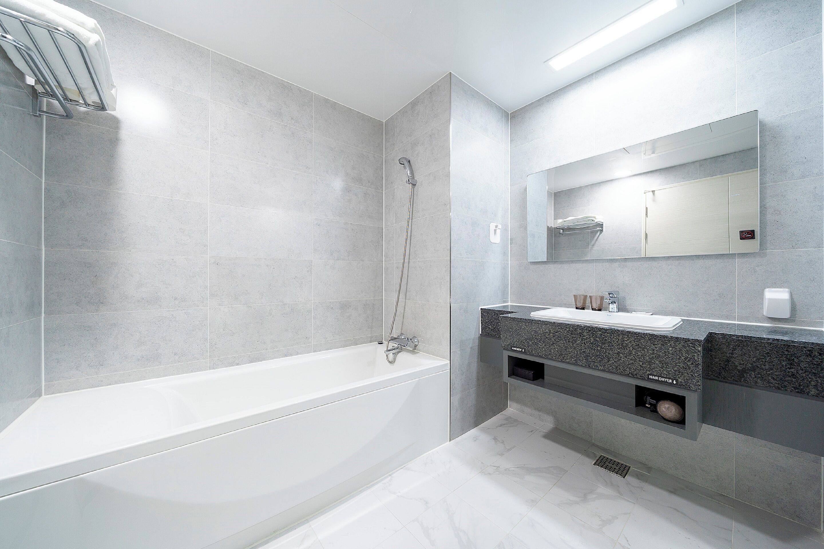 Un baño moderno con una bañera, ducha, tocador con espejo y un perchero para toallas.
