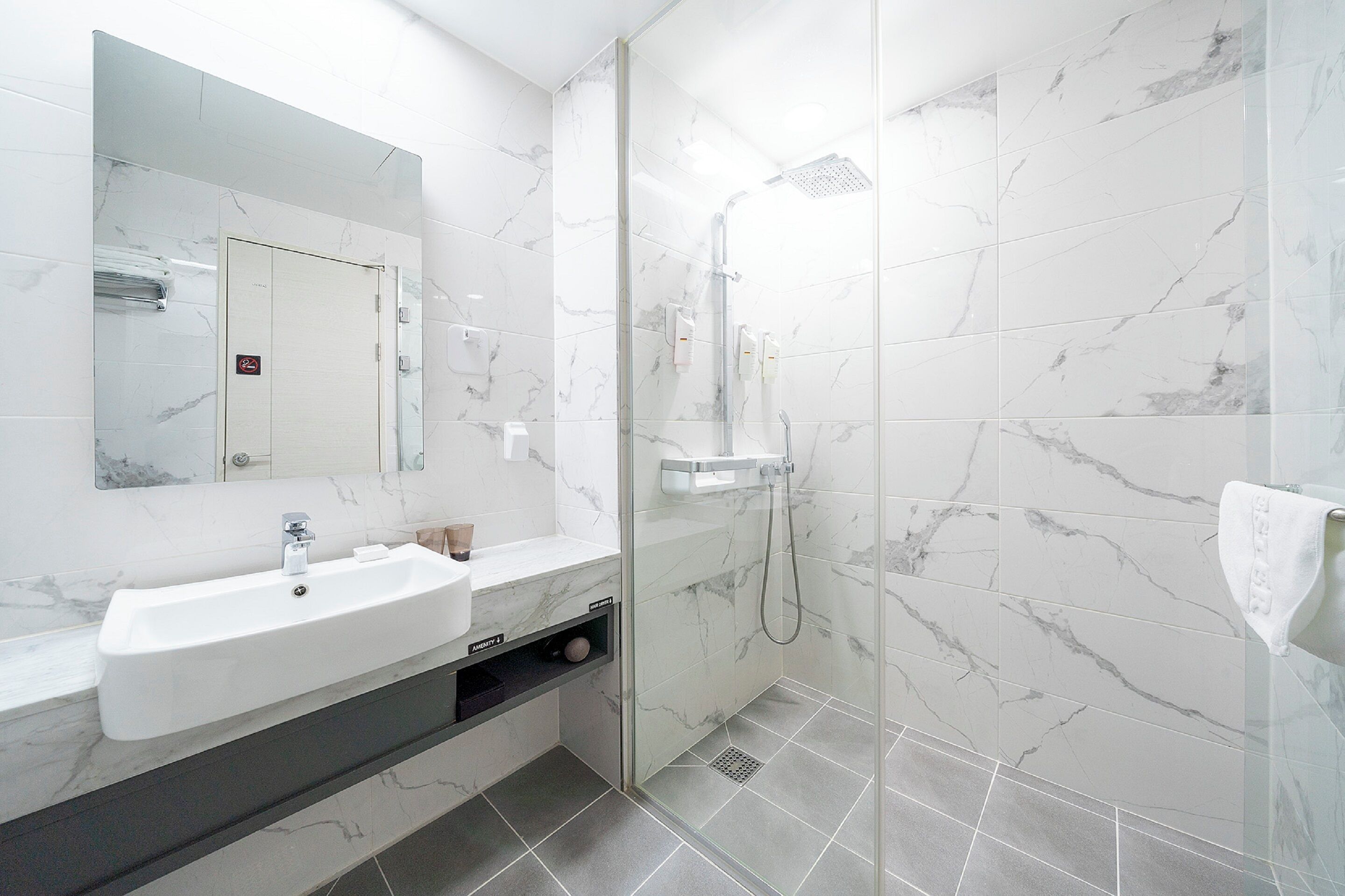 Un baño moderno con lavamanos de mármol, ducha con cerramiento de vidrio y un espejo grande.