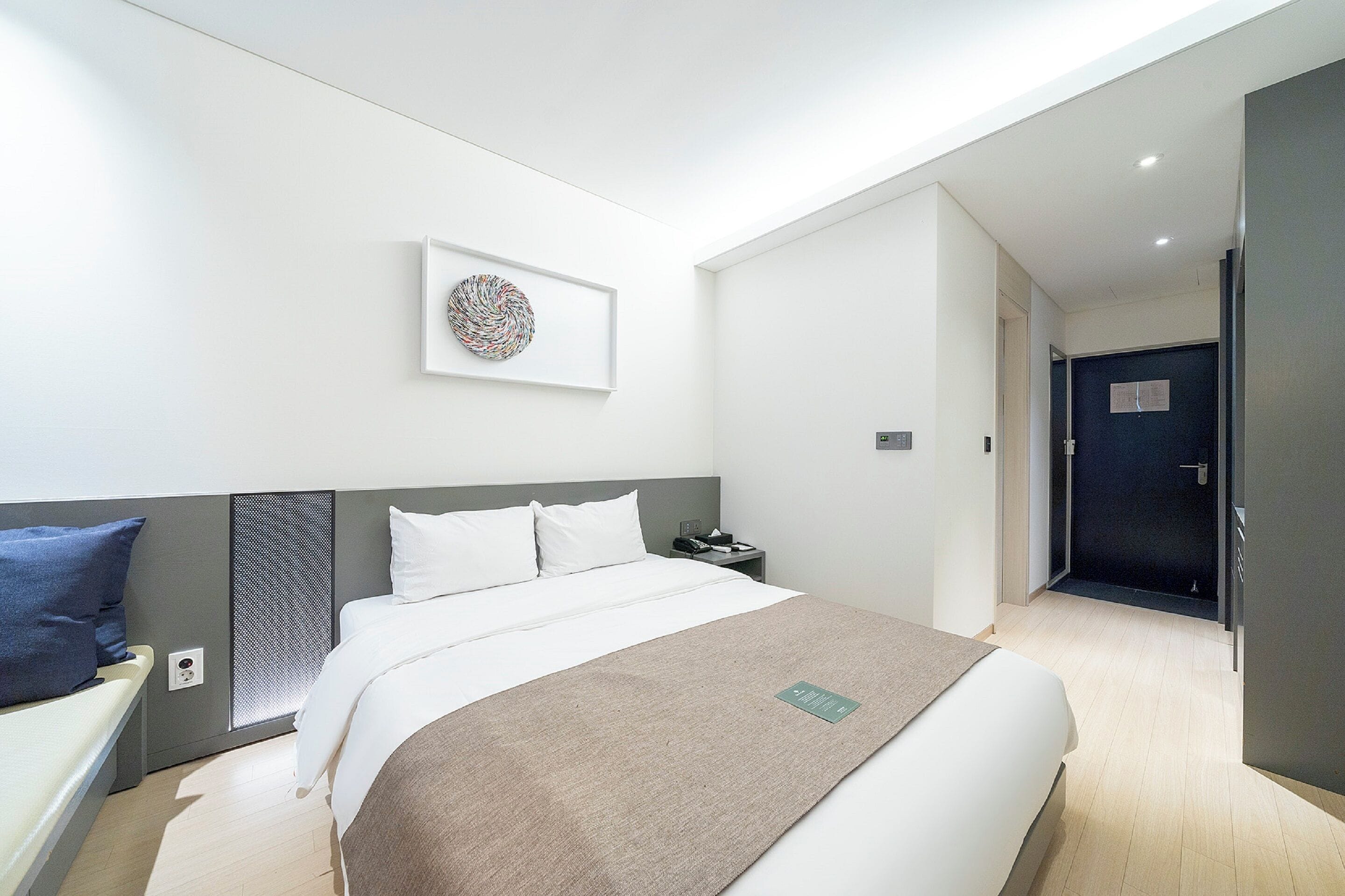 Una habitación de hotel moderna con una cama grande, una mesita de noche, una obra de arte colgada en la pared y una puerta que da a otra habitación.