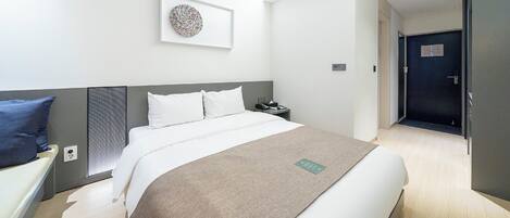 Una habitación de hotel moderna con una cama grande, una mesita de noche, una obra de arte colgada en la pared y una puerta que da a otra habitación.