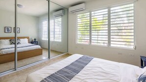 Een slaapkamer met een bed, een grote spiegel, een airconditioning en een raam met zonwering.