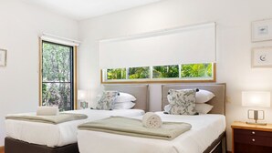 Habitación de hotel con dos camas, un ventanal con vistas a zonas verdes, una mesita de noche con lámpara y una obra de arte colgada en la pared.
