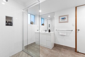 A modern bathroom with a glass shower enclosure, a white vanity with a mirror, and a framed picture on the wall.