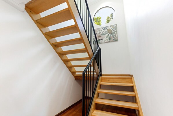 Una escala de fusta amb barana negra, que porta a un badiu amb un element decoratiu a la paret.