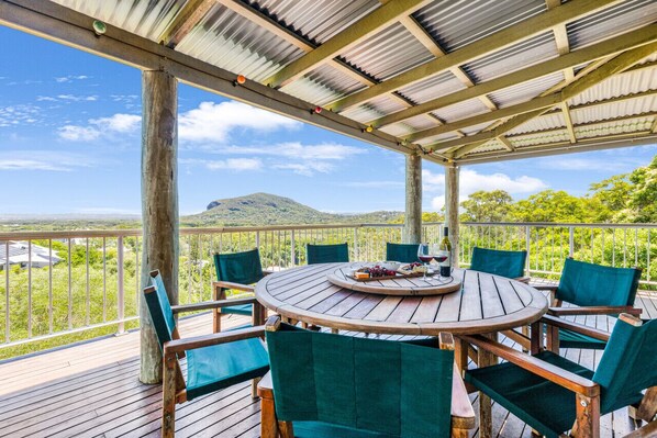 A covered outdoor seating area with a wooden table and chairs, overlooking a scenic landscape. - Breathtaking Panoramic Ocean Views (Point Arkwright)