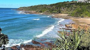 Paisaje costero con playa, costa rocosa y vegetación.