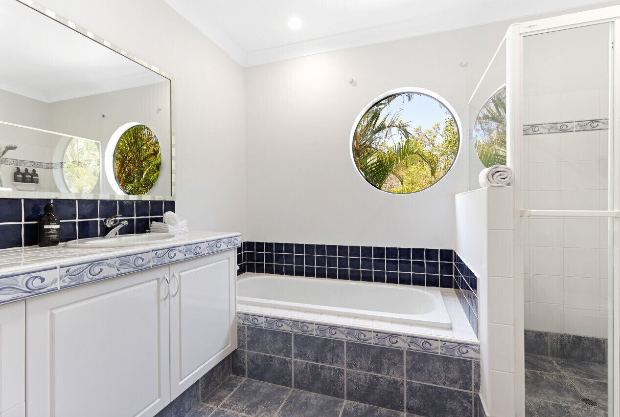 A modern bathroom with a bathtub, a large mirror, and two circular windows with tropical views.