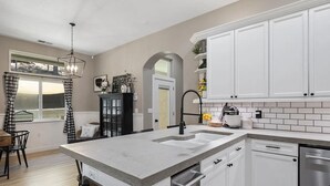 A modern kitchen with white cabinets, a large island, and a window with curtains. - Spacious-Gourmet Kitchen-Luxe King Bed-Ping Pong-Arcade (Sonora)