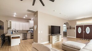 A spacious living area with a sofa, a TV on a stand, a kitchen with white cabinets, and a dining area with chairs. - Spacious-Gourmet Kitchen-Luxe King Bed-Ping Pong-Arcade (Sonora)