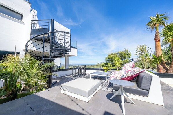 A rooftop terrace with a spiral staircase, outdoor seating, and a view of the ocean.