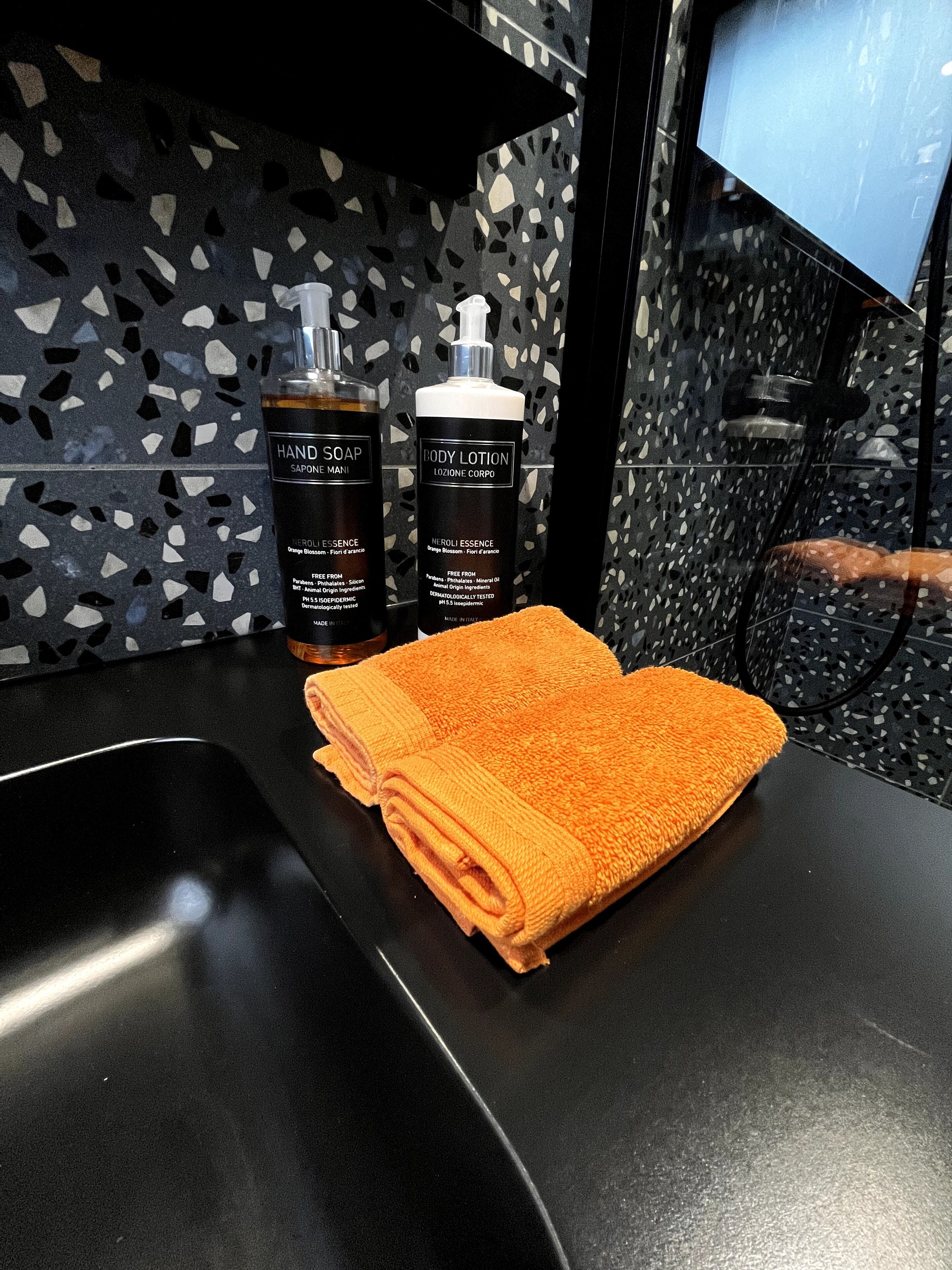 A bathroom with a black countertop, two bottles of hand soap and body lotion, and a folded orange towel.