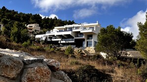 Un immeuble moderne à plusieurs étages, doté de balcons et entouré d’arbres et de rochers.