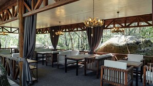 An outdoor seating area with wooden tables and chairs, draped curtains, and chandeliers. - Dom u ozera  (Burabay)