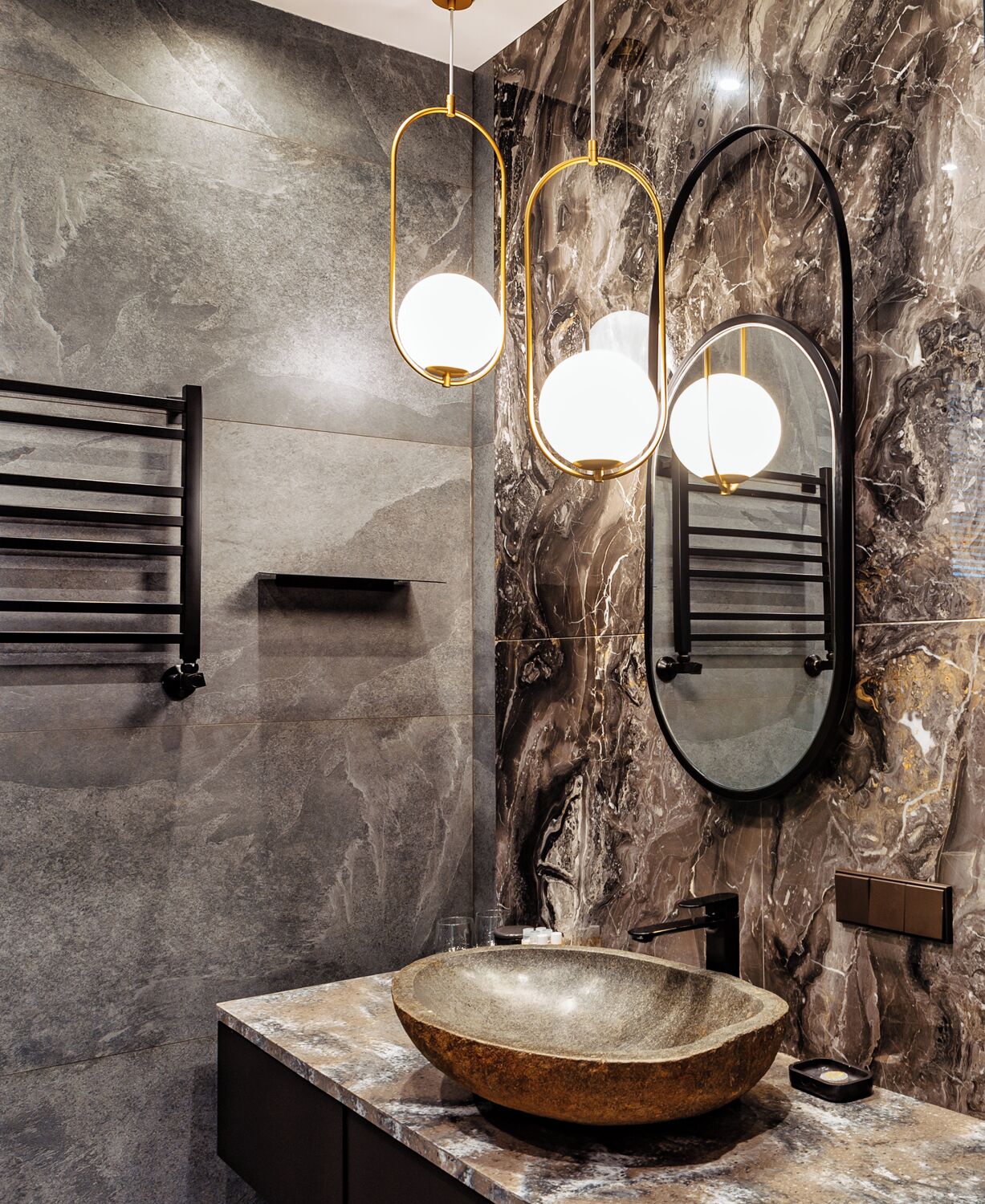 A bathroom with a large marble wall, a round sink, and two pendant lights.