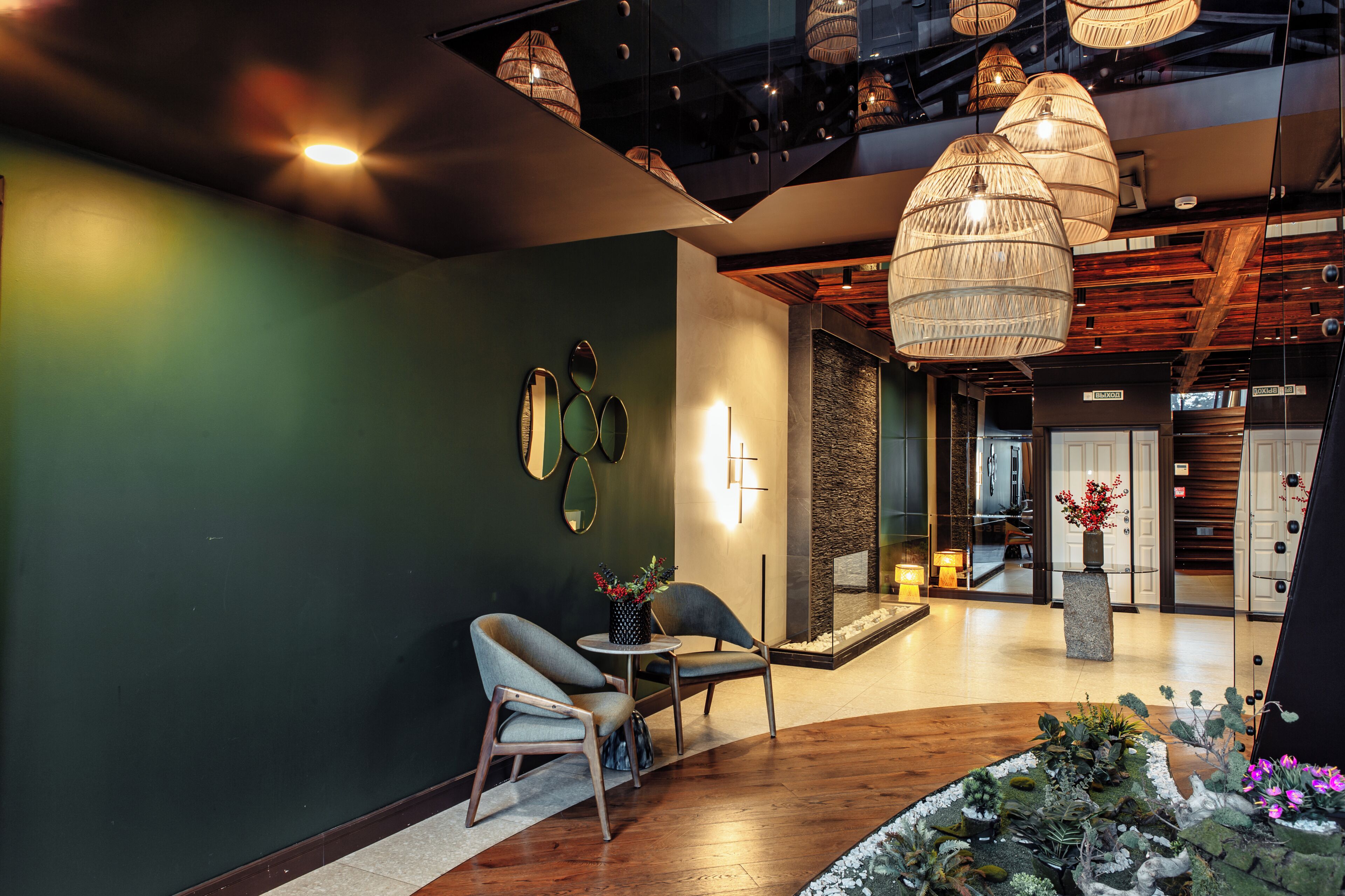 Eine moderne Lobby mit grüner Wand, Holzboden und einer Sitzecke mit zwei Stühlen und einem kleinen Tisch.