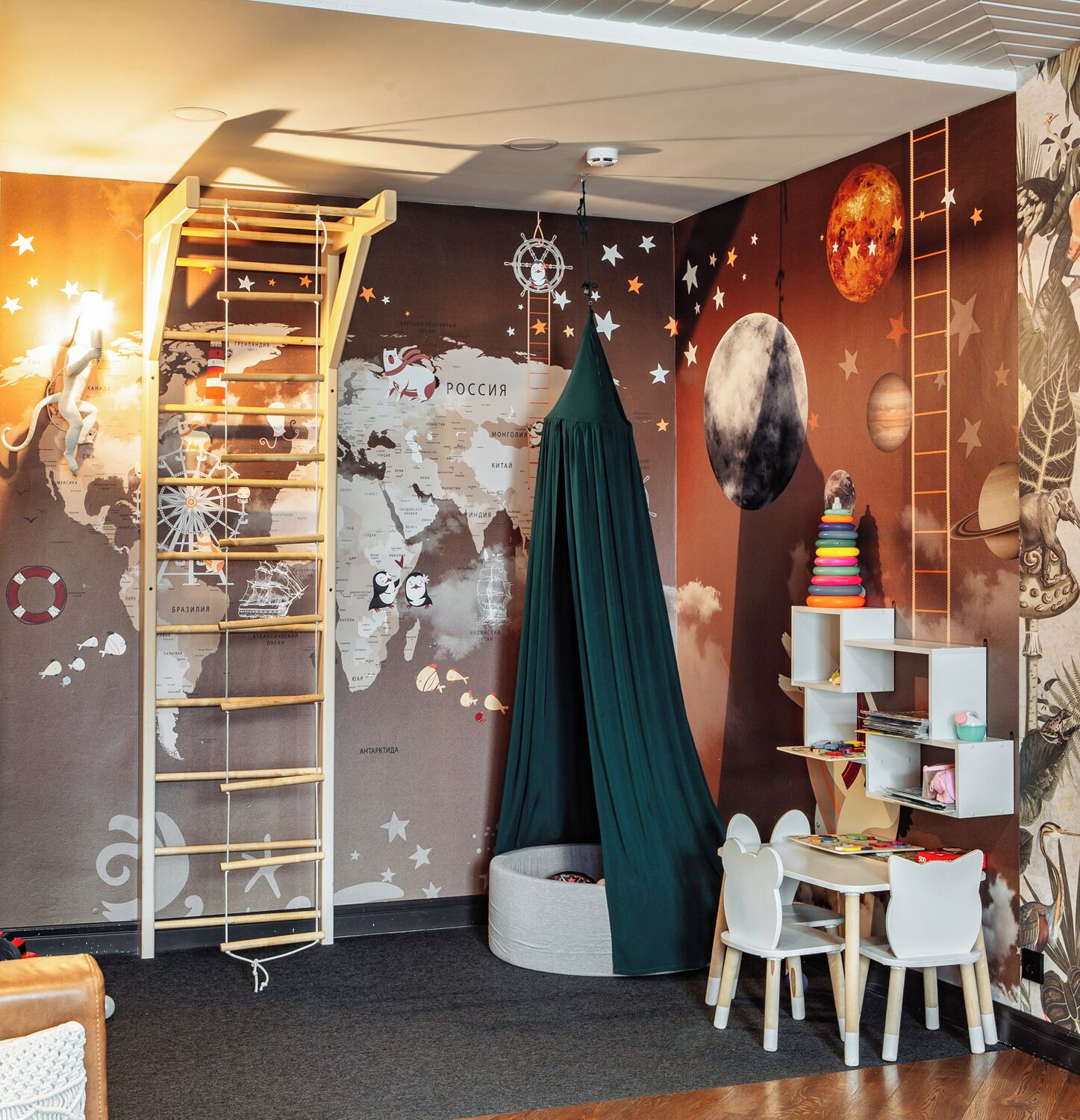 Une chambre d’enfant avec une carte du monde, une échelle, une tente verte, une bibliothèque et une petite table avec des chaises.