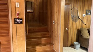 Eine Holztreppe führt zu einer oberen Etage, eine Holztür mit einem Foto, ein Tennisracket und ein Eimer auf dem Boden.