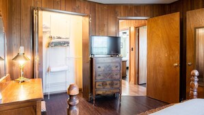 Ein Zimmer mit Holzwänden, einem Bett, einem Schminktisch, einem Fernseher und einem Kleiderschrank.