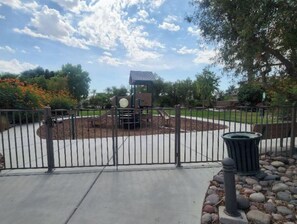 Guests can enjoy a secure outdoor playground with a slide and climbing elements surrounded by a beautifully landscaped area with trees and shrubs.