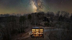Eine Hütte mit großem Fenster, einer Veranda und Blick auf die Milchstraße.