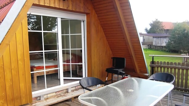 A wooden deck with a glass table and chairs, a sliding glass door, and a small table with a chair. - Holiday home in Thale in the Harz Mountains (Thale ot Allrode)