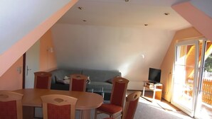 A dining area with a table and chairs, a sofa, a television, and a sliding glass door leading to a balcony. - Holiday home in Thale in the Harz Mountains (Thale ot Allrode)