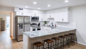 A modern kitchen with white cabinets, stainless steel appliances, a marble island, and bar stools.
