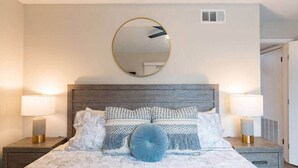 A bedroom with a wooden headboard, two bedside lamps, a round mirror, and patterned bedding.