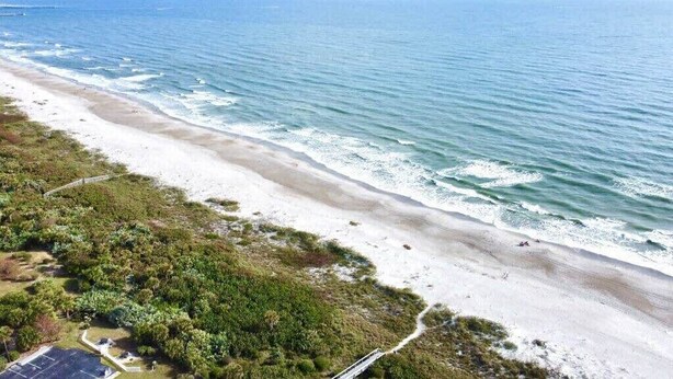 An aerial view of a beach with a parking area and a path leading to the shore.