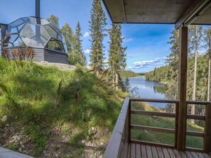 A wooden deck overlooking a lake with a glass structure on a grassy hill.