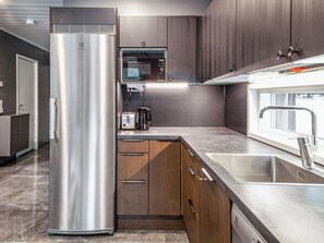 A modern kitchen with stainless steel appliances, wooden cabinets, and a built-in microwave. - Villa ukkometso by Interhome (Kuusamo)