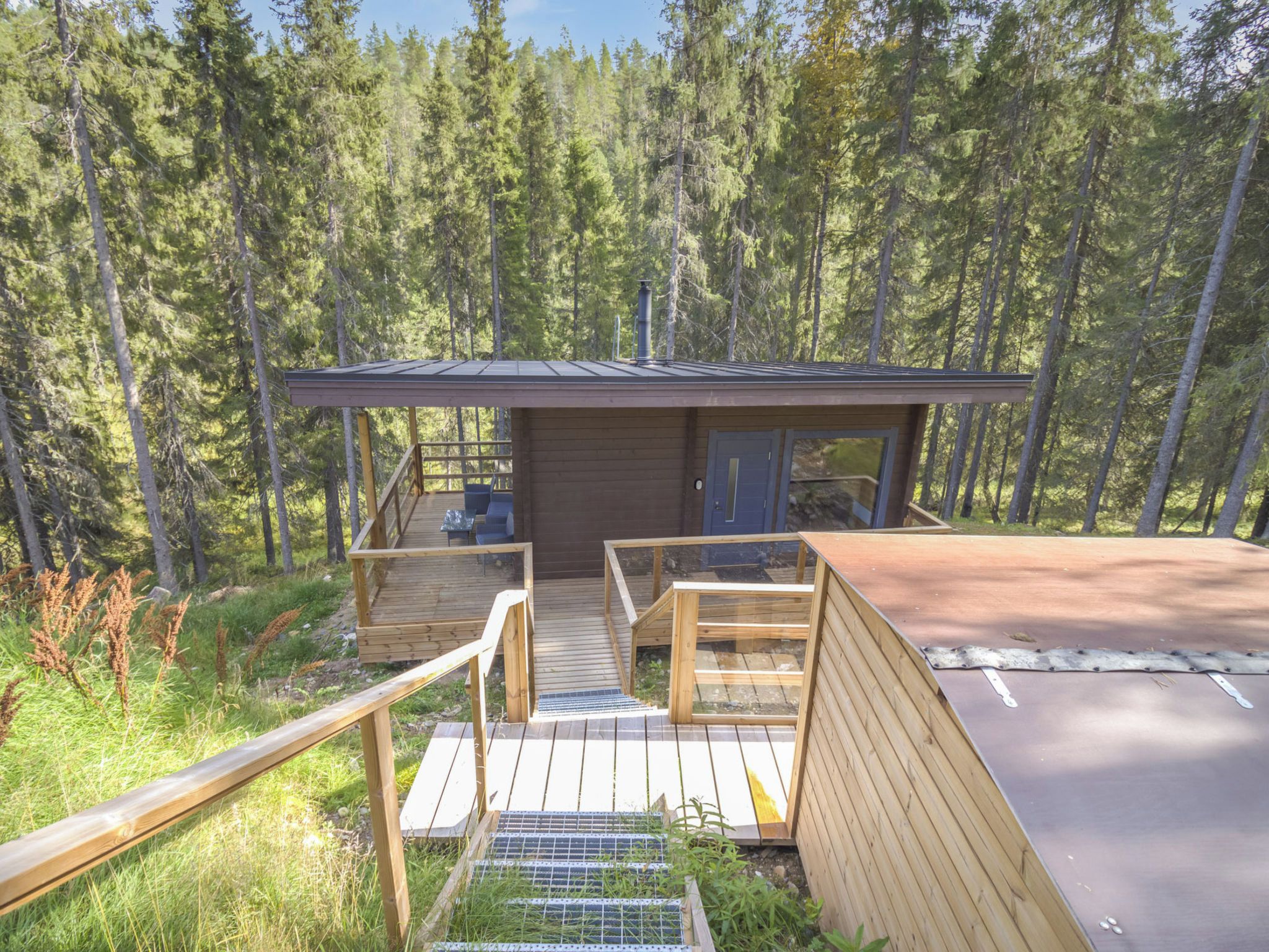 A cabin with a deck, a covered outdoor seating area, and a view of a forest.