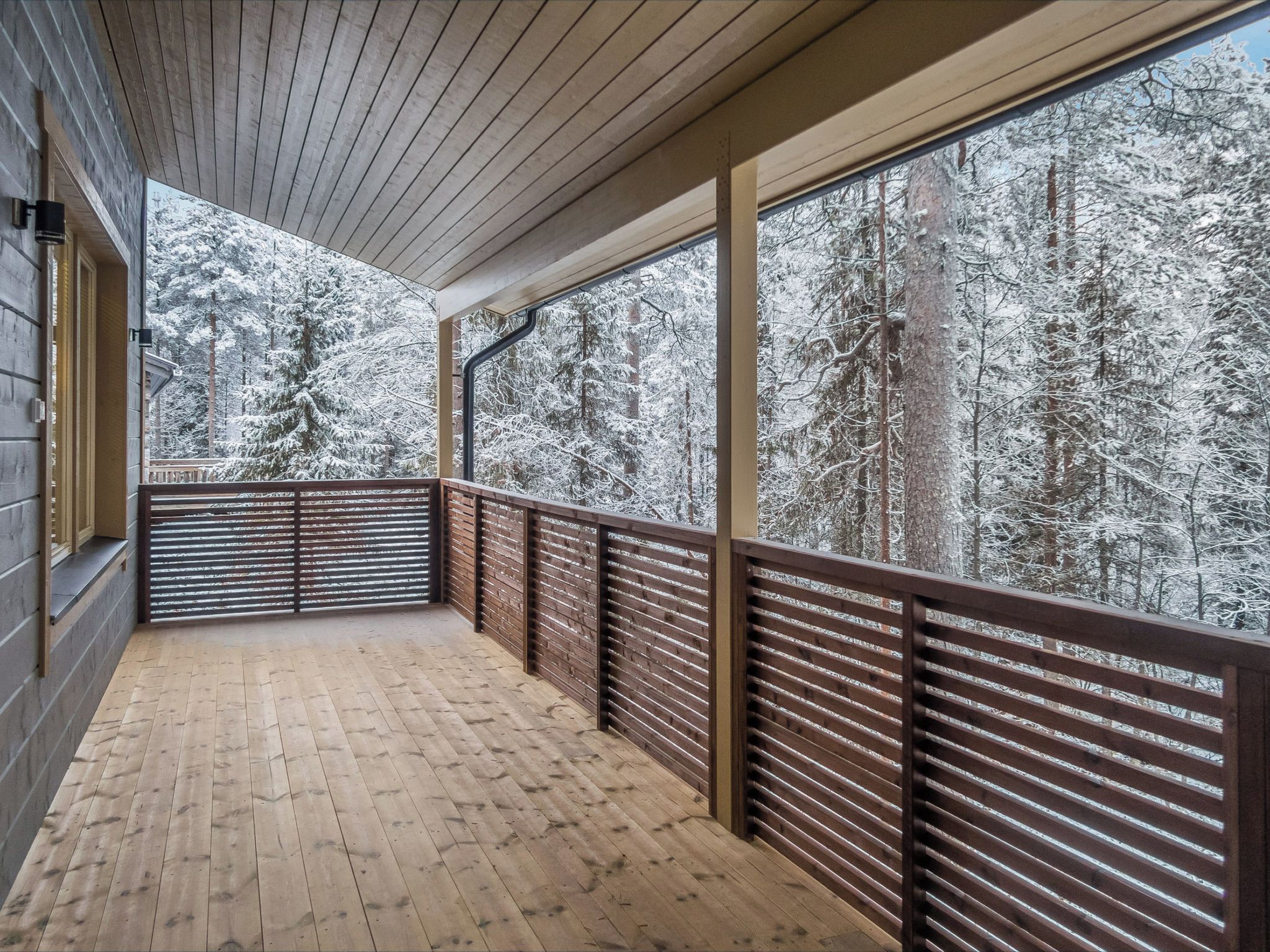A wooden deck with a view of snow-covered trees.